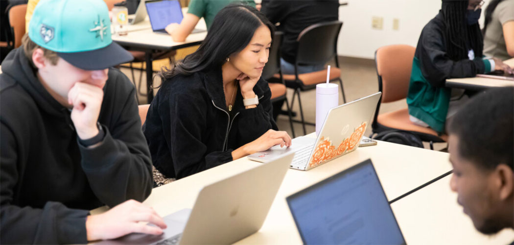 Three students sitting at a table all working on computers