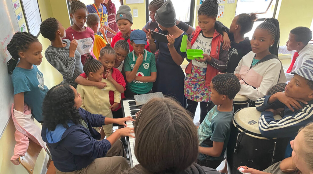 Student plays piano as students stand around