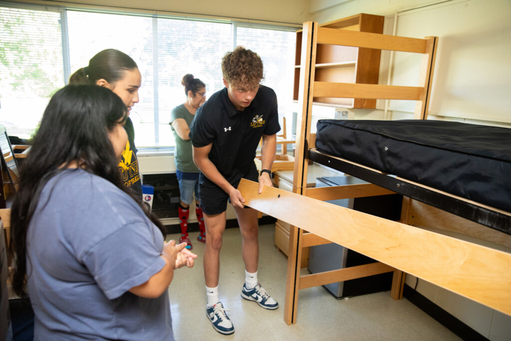 Student helps another student make a bed while student and parent watch.