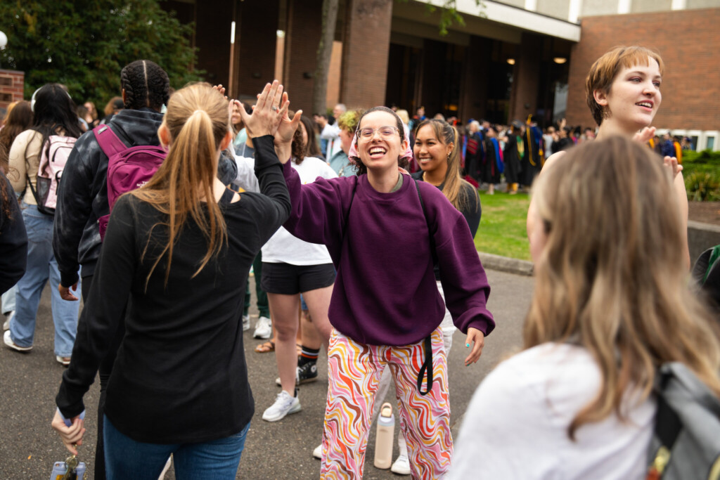 Student high fives another student as they walk through a line outside.