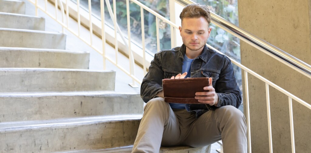 Gavin Ripka sits on steps in a building on campus while working on an tablet