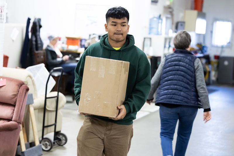 A student carries a box while helping sort and organize furnishings at Northwest Furniture Bank during a J-Term on the Hill class.