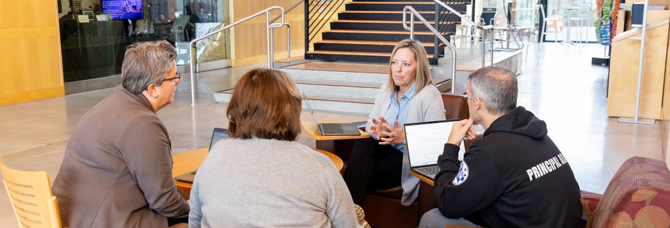 A group of four EdD student sit at a small table for discussion in the large lobby of PLU's Morken Center for Learning and Technology.