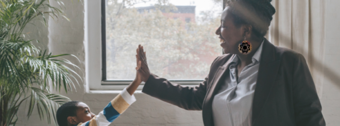 An adult and a kid high five in front of a large window. Also visible is a plant.