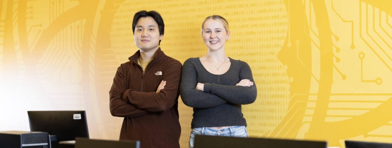 Two students stand in a computer science classroom