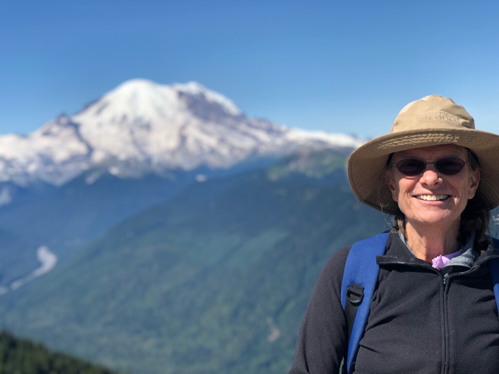 Dr. Romey Haberle wearing a hat and sunglasses with Mount Rainier in the background.