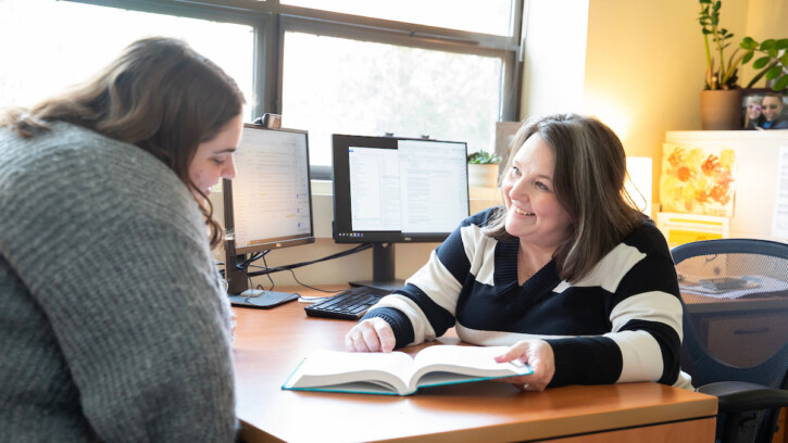 Professor Tiffany Artime sitting at her desk talking to a student.