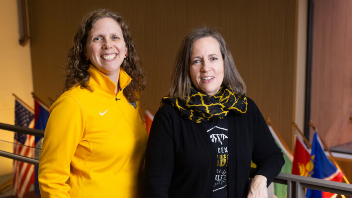 Dr. Ann Auman and Dr. Bridget Yaden pose in front of international flags.