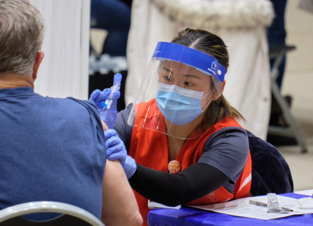 Wearing a mask, face shield and other nursing attire, a PLU nursing student administers a COVID-19 vaccination.