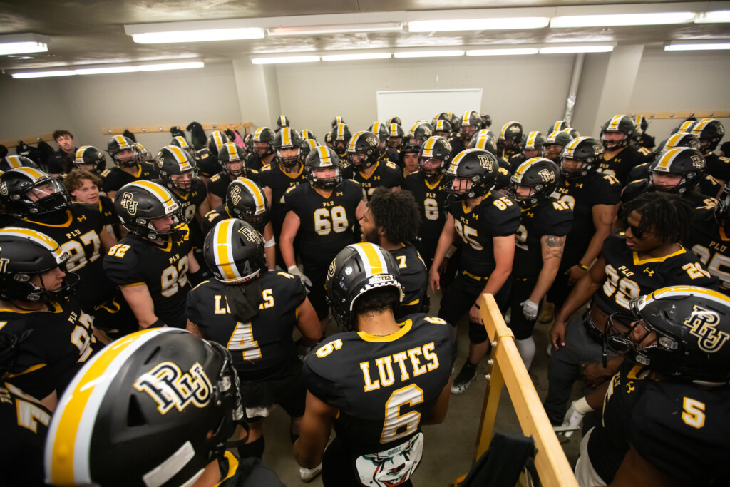 Football players stand in a big group in the locker room before a game.