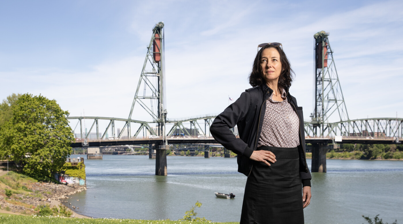 A person stands in front of the water front in Portland looking into the distance.