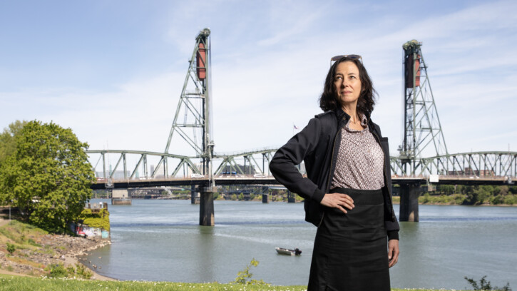 A person stands in front of the water front in Portland looking into the distance.