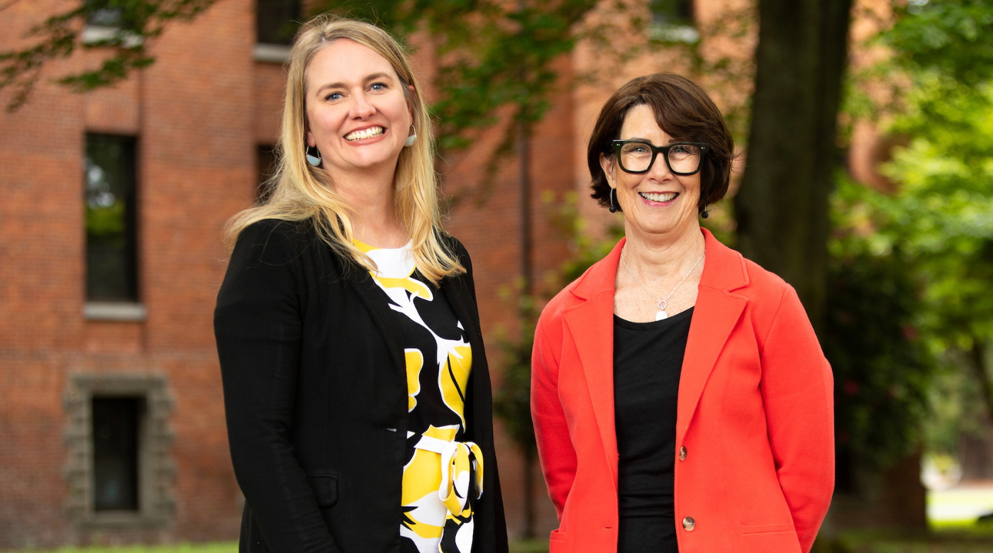 Two PLU staff members smile into the camera while standing outside.