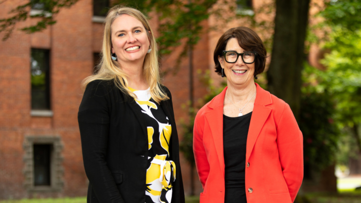 Two PLU staff members smile into the camera while standing outside.