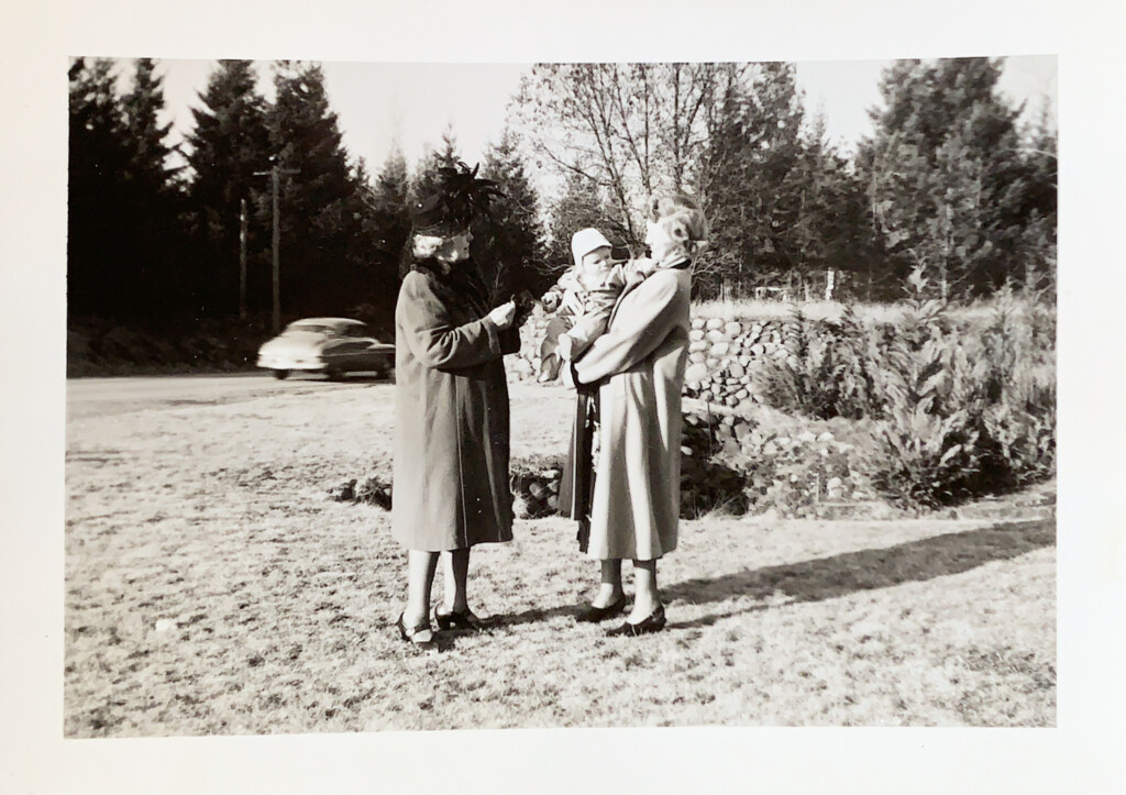 Two women stand outside in a black and white photo holding a baby