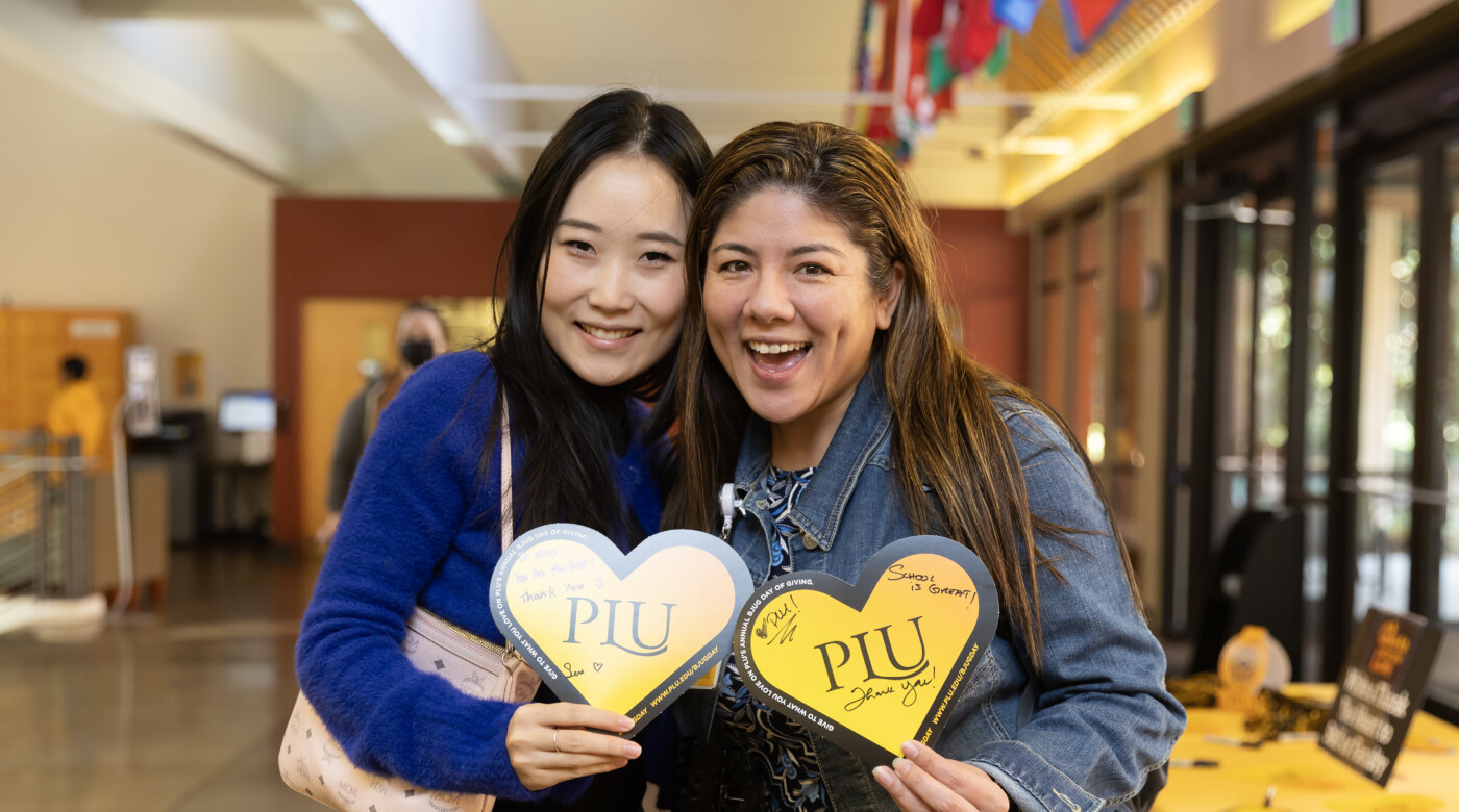 Two students hold hearts and smile into the camera.