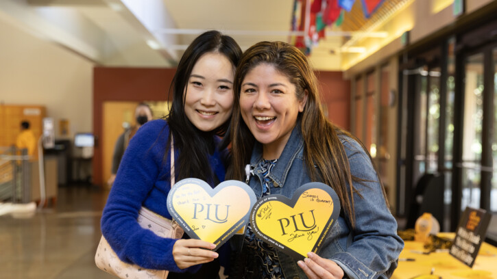 Two students hold hearts and smile into the camera.