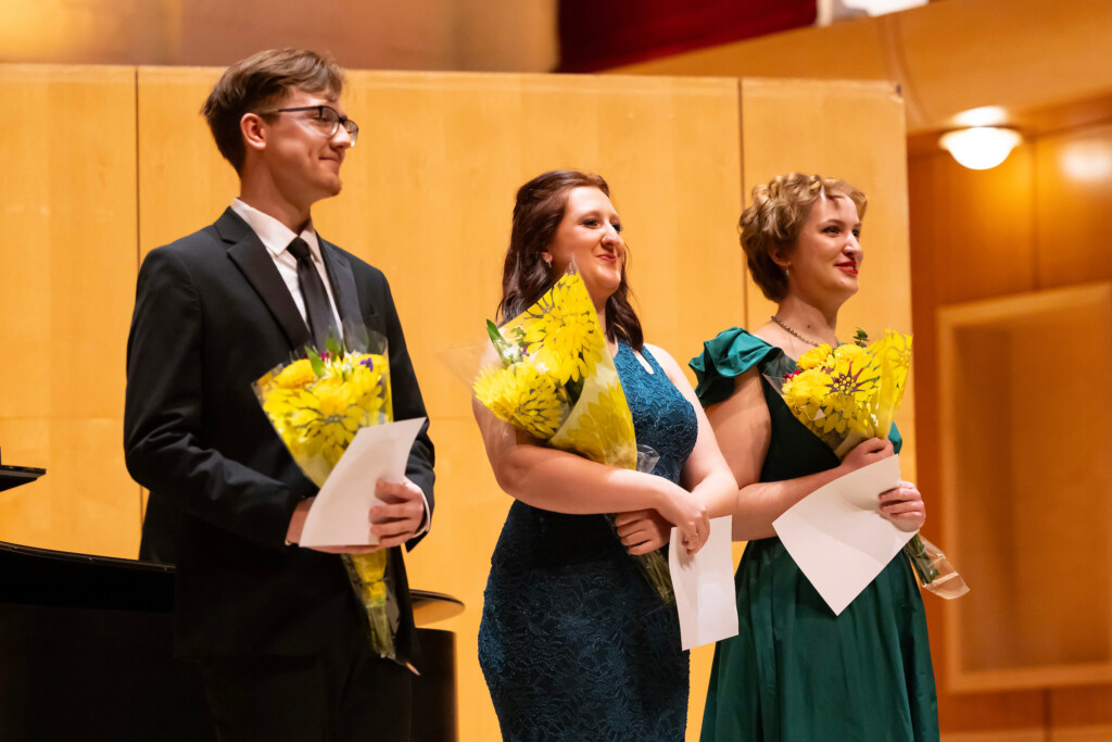 Three winners stand in front of a piano.